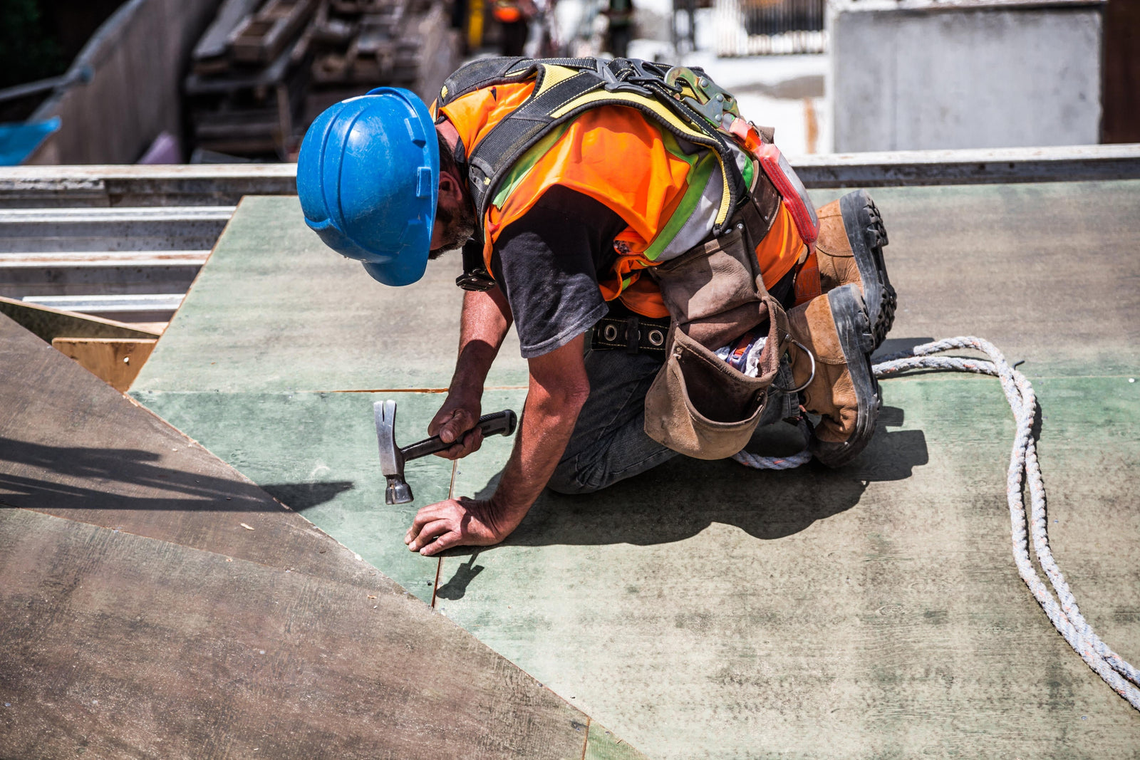 A construction worker, who has one of the common high risk jobs, is nailing a wood board using a hammer on a roof