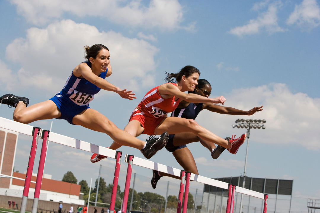 Three female athletes who have incorporated liquid collagen supplements into their diets jump over a hurdle