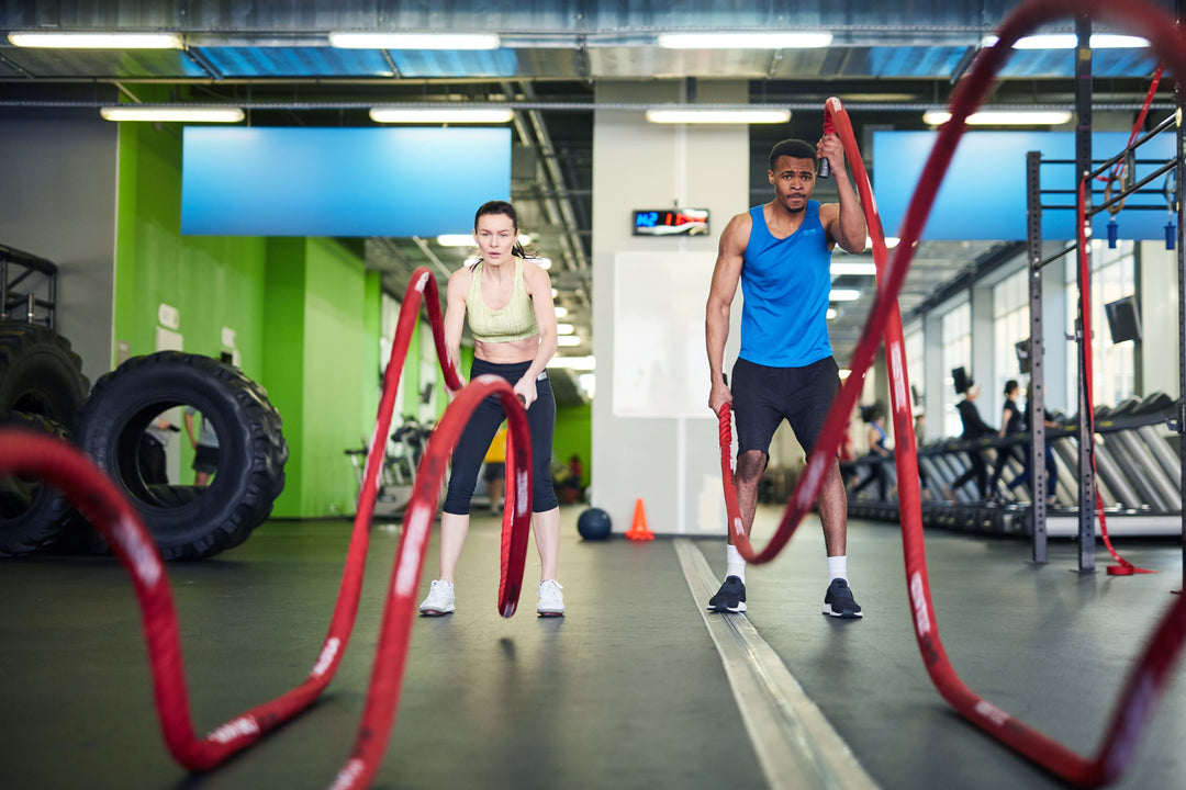 Athletes familiar with the best time to drink a protein shake are working out with battle rope in a gym