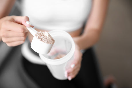 Sporty young woman aware of the cons of protein powder is holding a measuring scoop with collagen powder and a shaker bottle