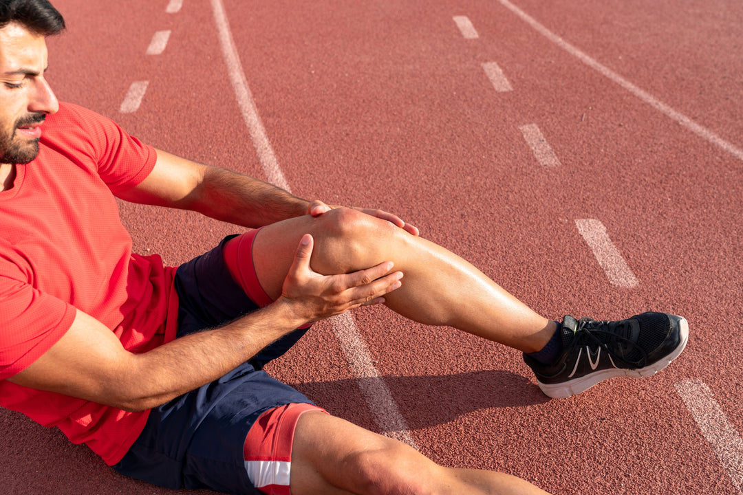 Injured male athlete sitting on the running track needs to undergo torn ACL treatment