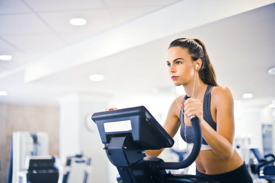 Female athlete listening to a podcast about hydrolyzed collagen benefits while working out on a treadmill in a well-lit fitness center