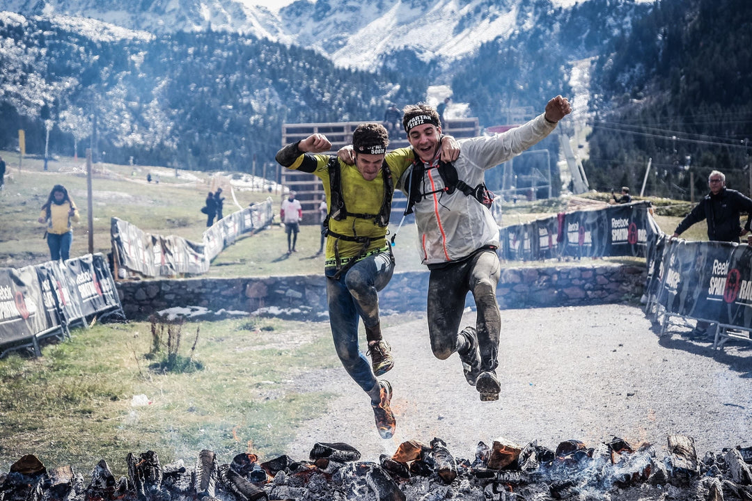 Two male athletes who understand the benefits of collagen supplementation are jumping over hot coals during a spartan race